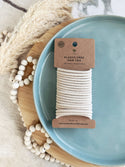 A bundle of plastic-free hair ties in blonde/tan color, displayed on a blue plate with a cardboard packaging label that reads 'Plastic-Free'. The hair ties are made from cotton and natural rubber, and the label indicates the brand 'Me Mother Earth'.