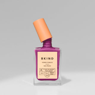 A bottle of BKIND nail polish in a vibrant plum purple shade, with a clear liquid visible inside the bottle and a purple cap on top.