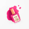 A bottle of BKIND nail polish in a vibrant fuchsia color with a pink tint, placed on a white surface, accompanied by a splash of the same color polish.