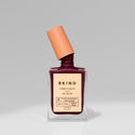 A bottle of BKIND nail polish in a dark purple shade with a glossy finish, featuring a brush applicator and labeled as vegan and 21-free.