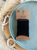 A bundle of black plastic-free hair ties placed on a blue plate, with a cardboard packaging label indicating the product is plastic-free and made with natural materials.